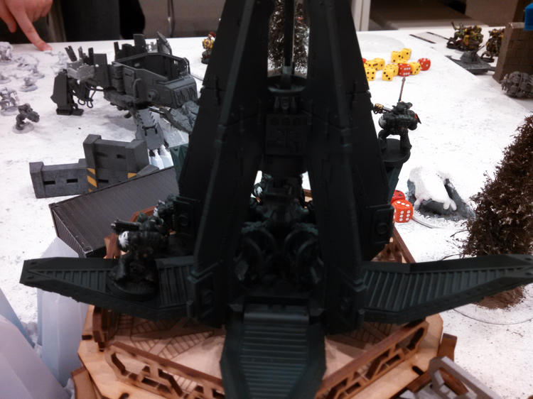 A close view of a large dark miniature and a Space Marine on the battlefield